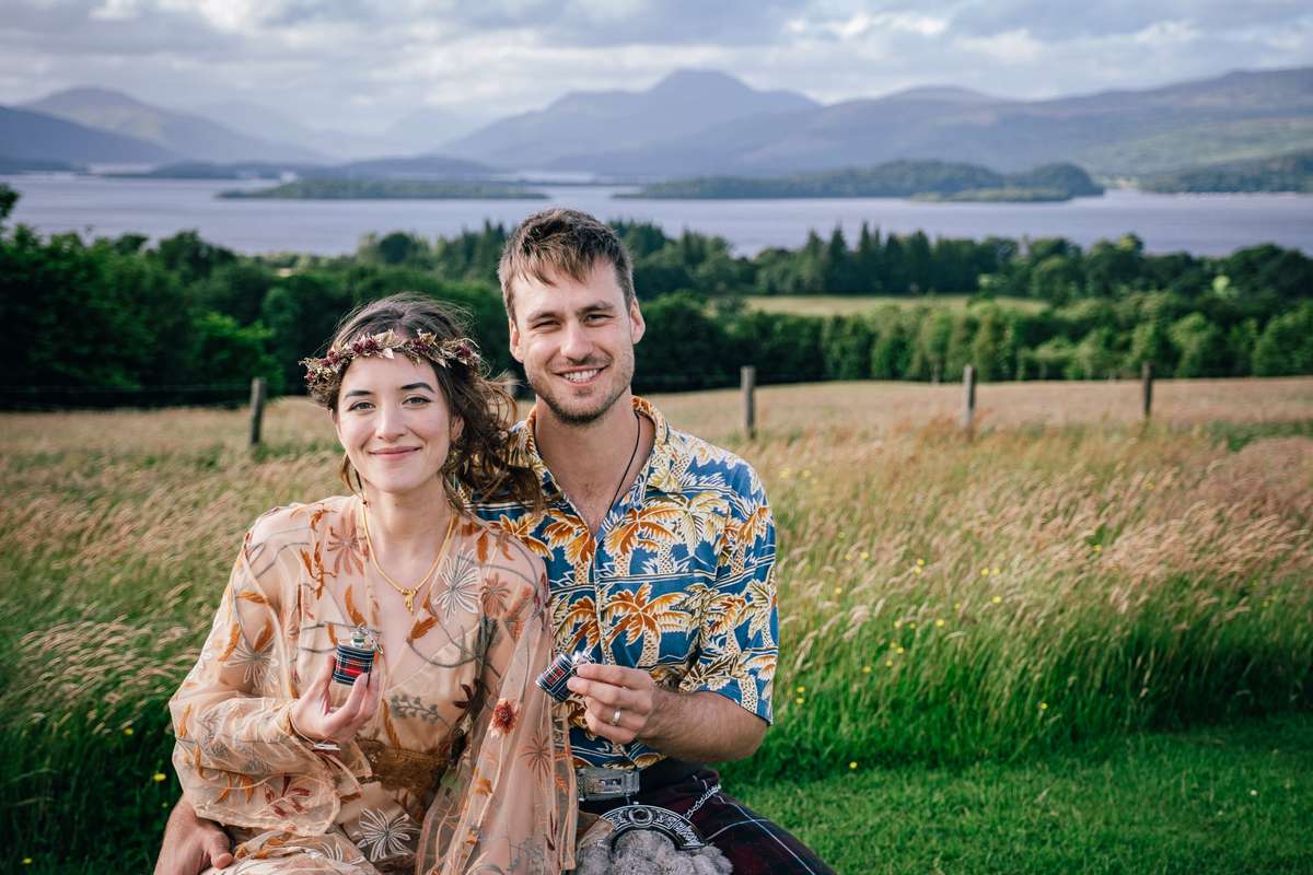 Newlyweds sitting together in the grounds of Ardoch Loch Lomond with the loch and mountains behind
