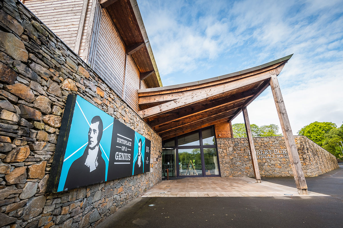 Entrance to the Robert Burns Birthplace Museum in Alloway, featuring stone walls, wooden architecture and outdoor signage.