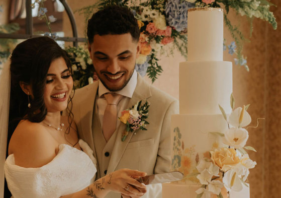 A bride and groom smile as they cut into their four tier wedding cake