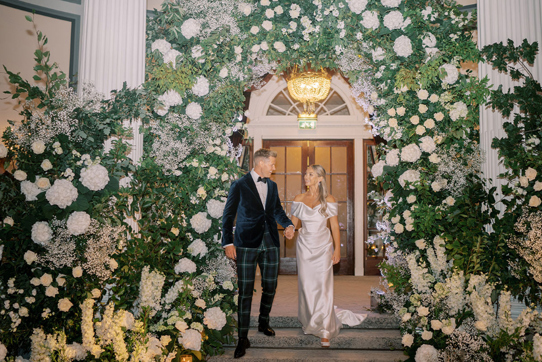 Bride and groom walk downstairs with white flower installation behind them