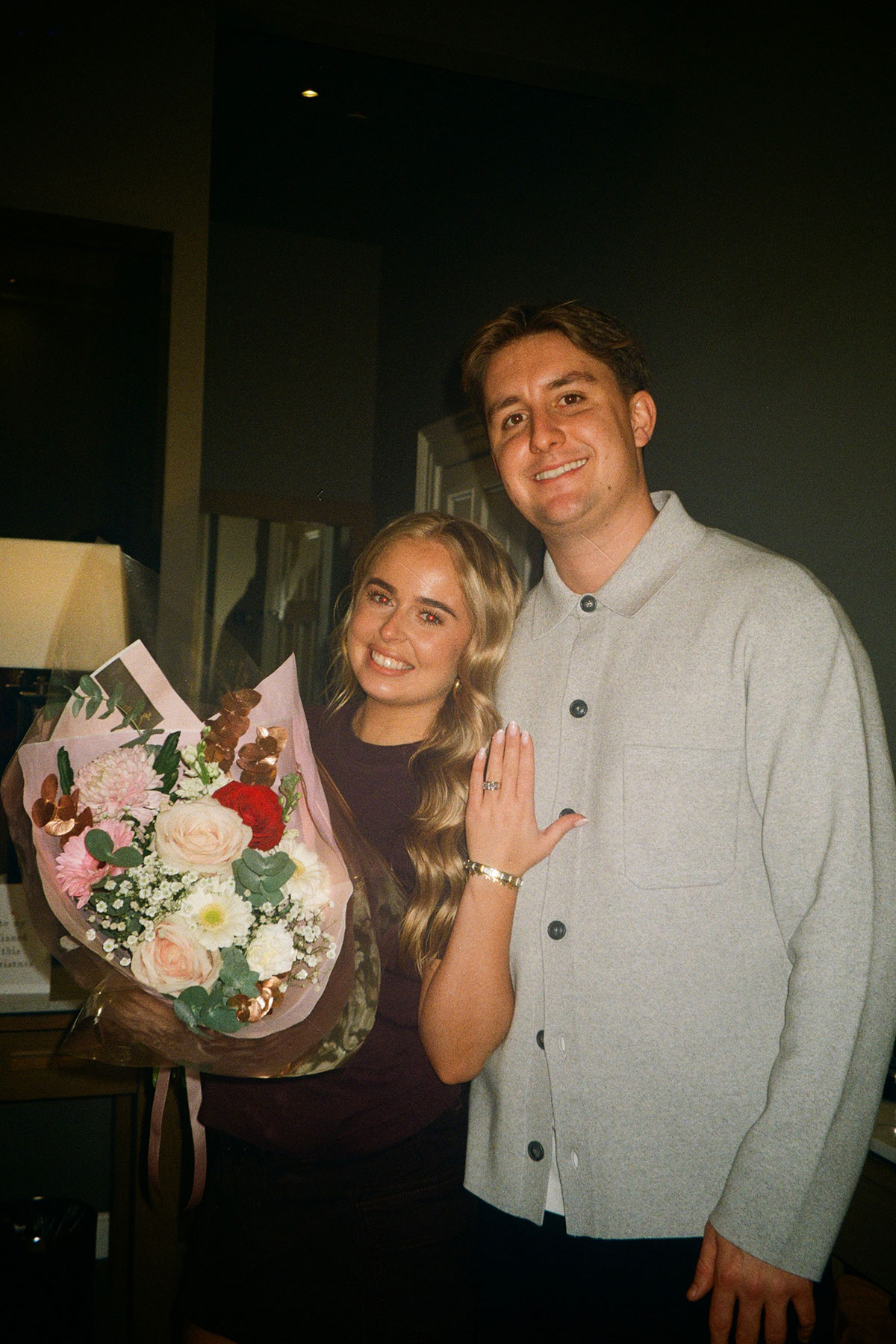 Ruby McFarlane holding a bouquet and showing her engagement ring while standing with Oskar Wilkie after their proposal.