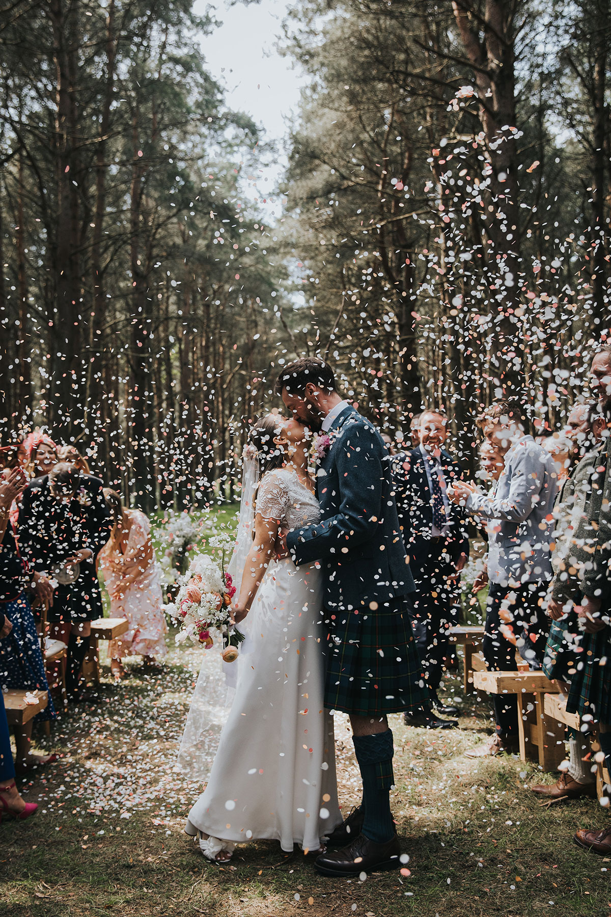 bride and groom share first married kiss as guests through wedding confetti over them