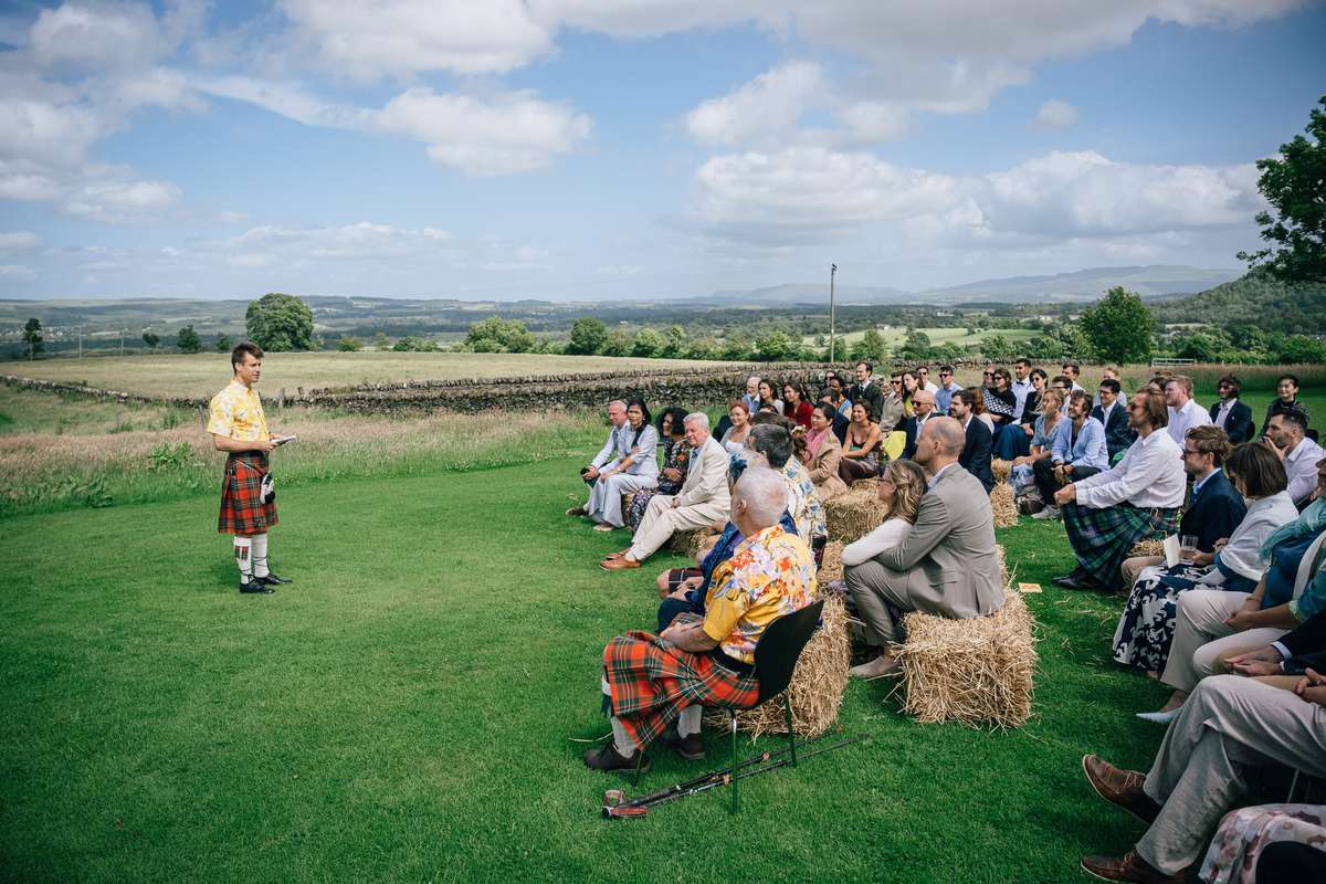 Outdoor wedding ceremony at Ardoch Loch Lomond with guests seated on hay bales in the countryside