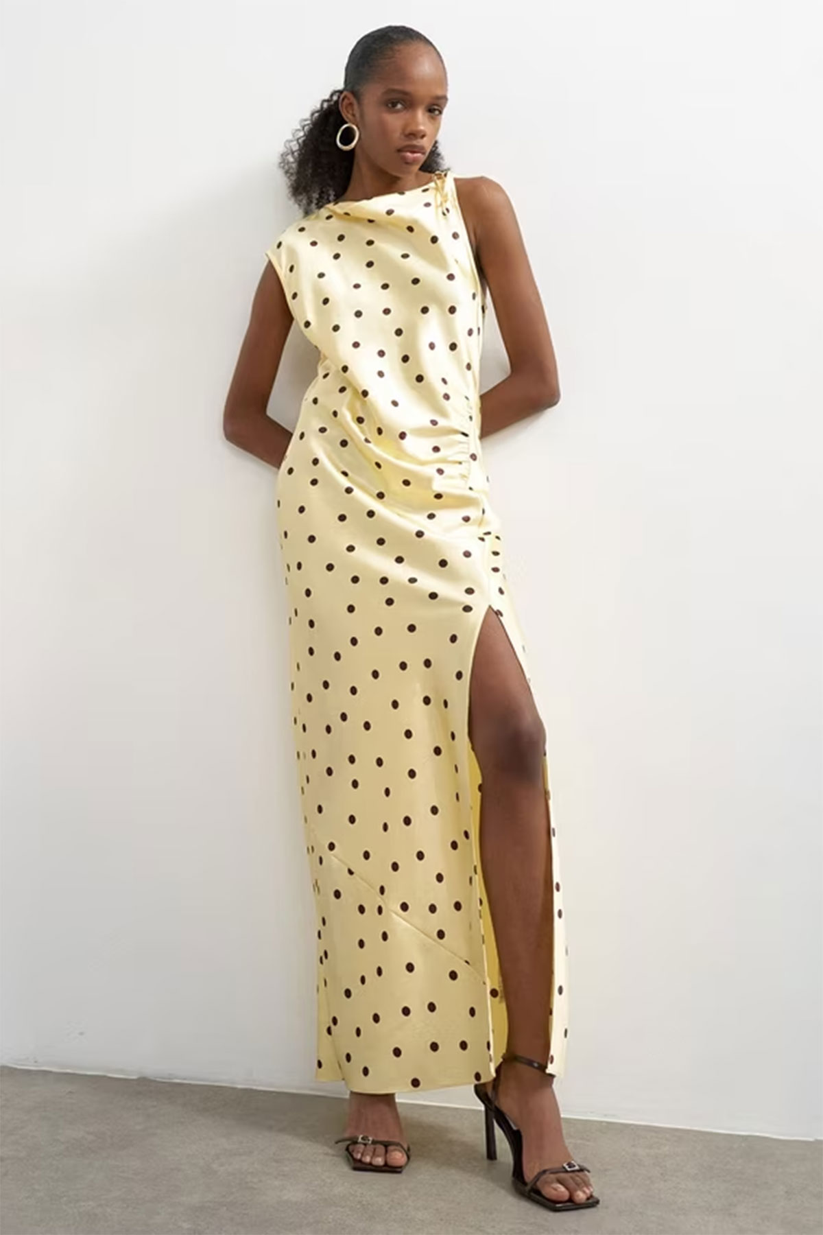 Yellow polka dot satin maxi dress with side slit and draped bodice styled with black heels