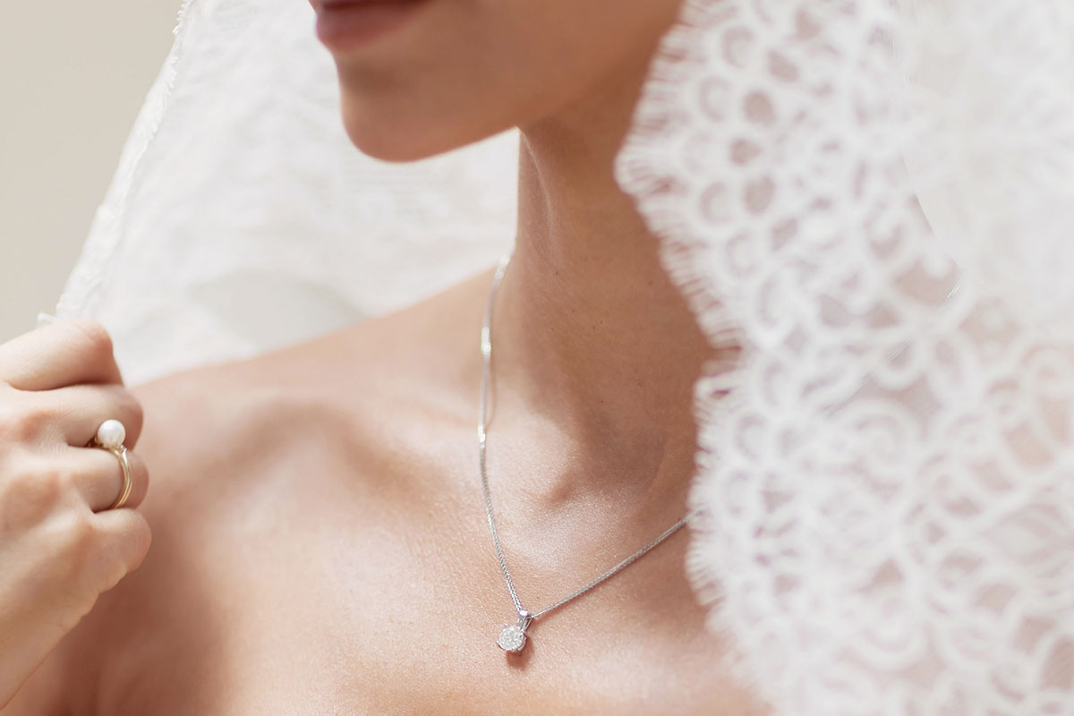 A close up of a bride's chest. She is wearing a diamond solitaire pendant