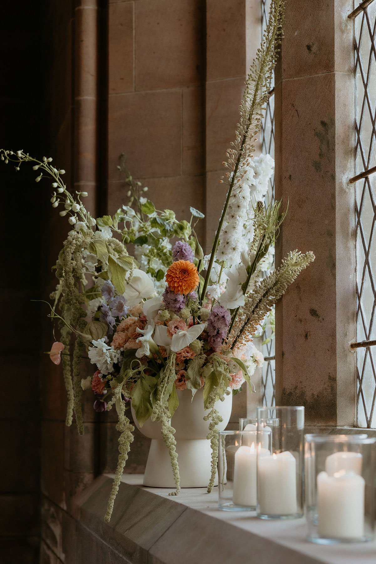 Romantic floral arrangement with candles on chapel window ledge at Rosebery House and Steading, Midlothian wedding venue.