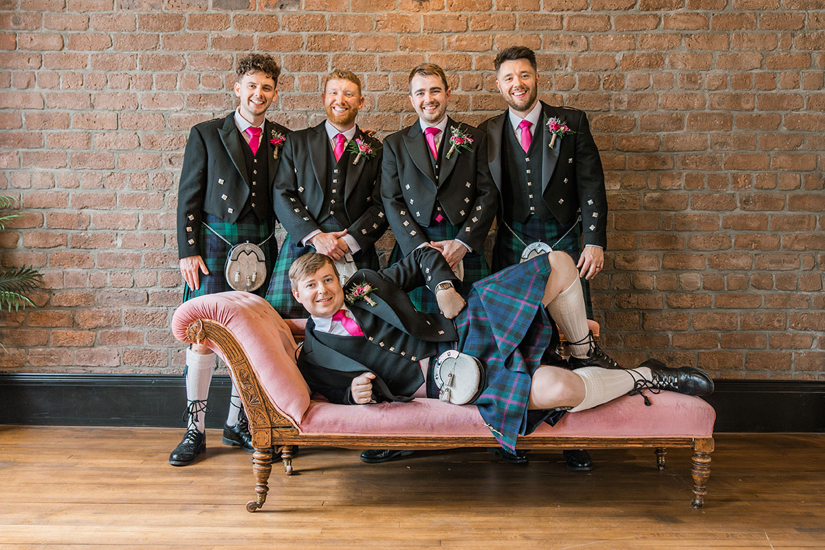 Groom posing with his groomsmen wearing matching tartan kilts