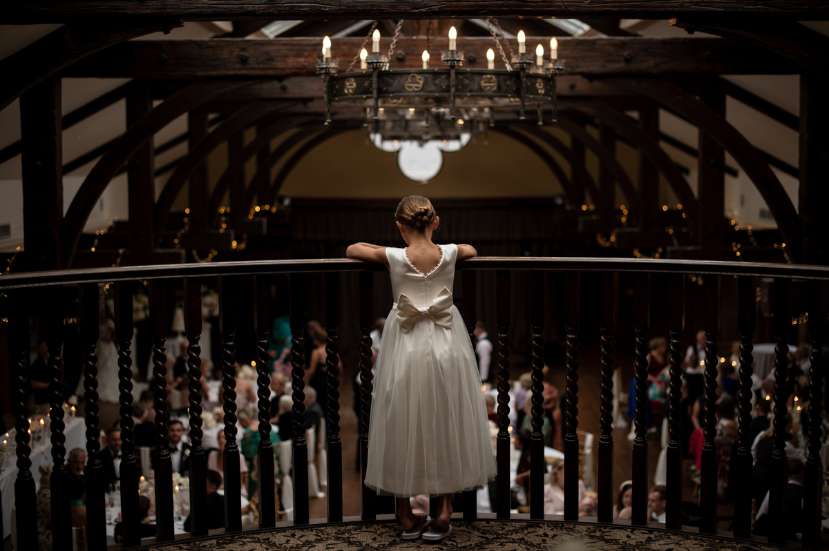 Flower girl in a white dress looking over the balcony during the wedding reception at Crossbasket Castle.
