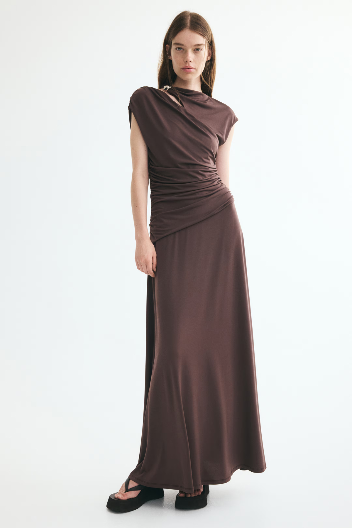 Model wearing a chocolate-brown draped maxi dress with a shoulder cut-out, ruched waist and cap sleeves.