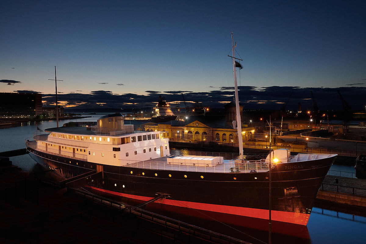 Exterior view of Fingal floating hotel in Leith, Edinburgh, illuminated at dusk with reflections shimmering on the water