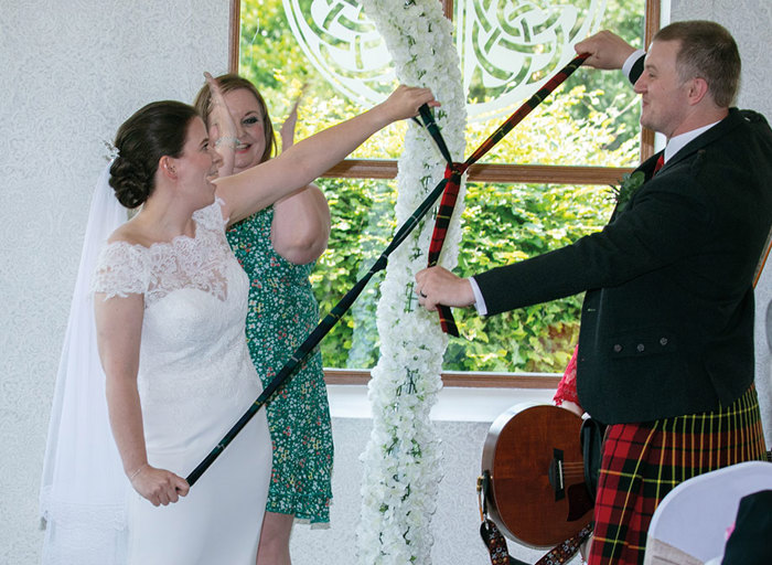 bride and groom doing handfasting with celebrant in the background clapping