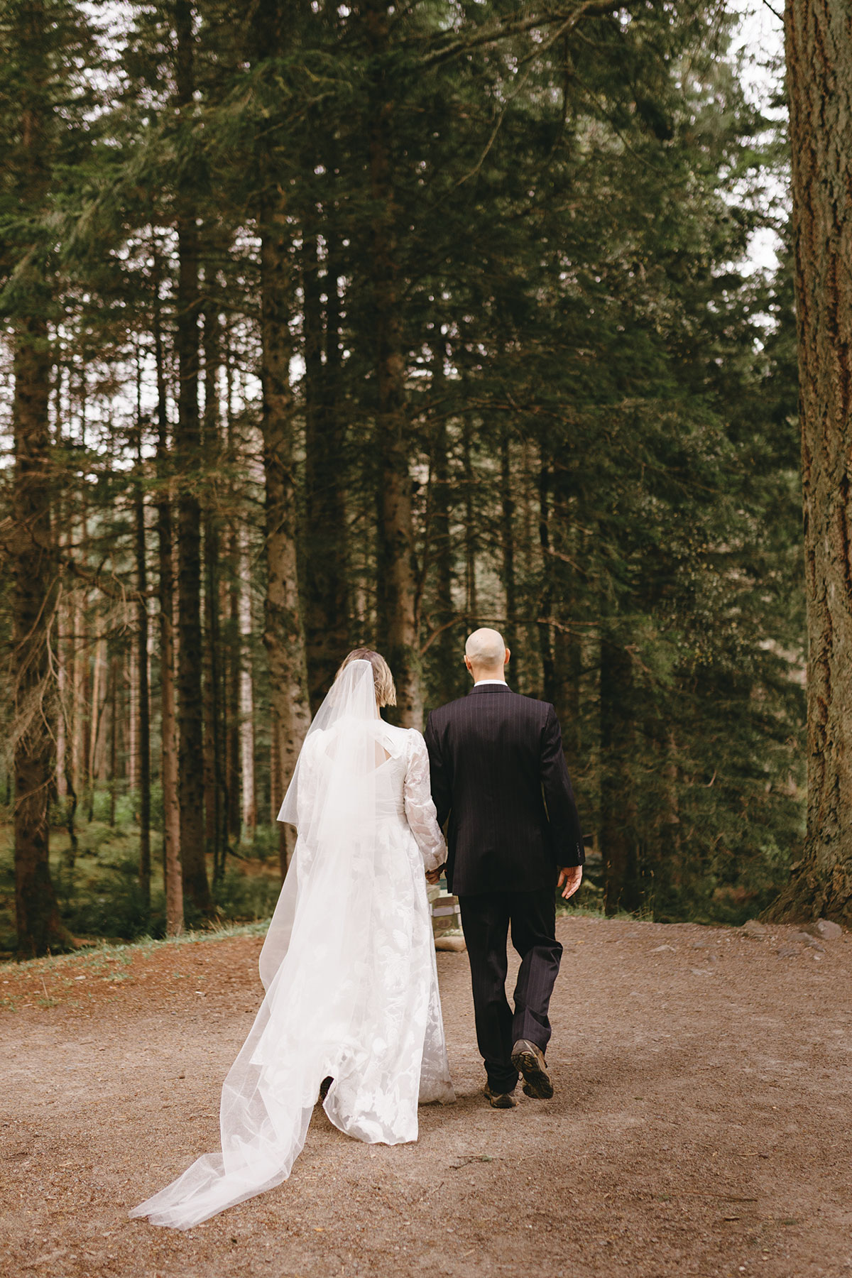 bride and groom walk towards forest on their wedding day