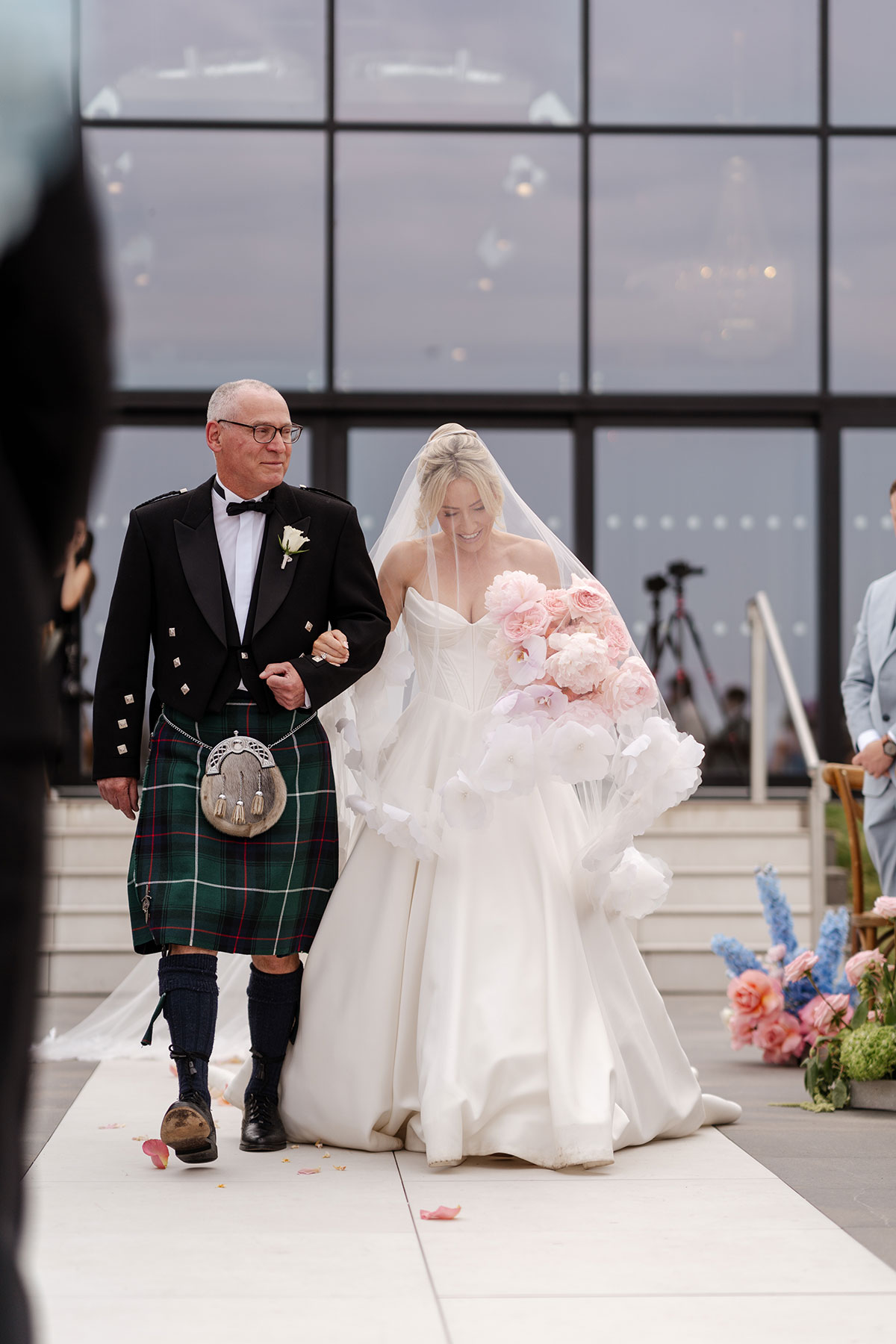 Bride walks down the aisle with her father during an outdoor wedding ceremony at Boturich Castle overlooking Loch Lomond.