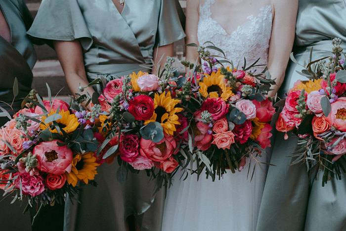 four colourful bouquets of flowers being held by a bride and three bridesmaids