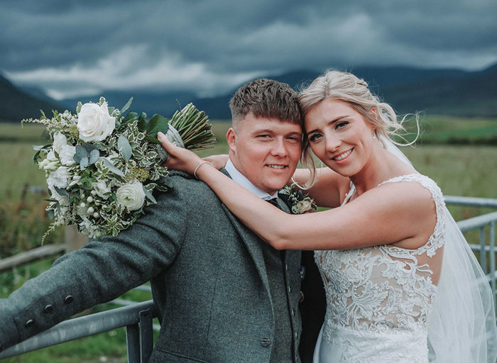 a bride and groom posing standing against a metal gate with moody grey skies in background