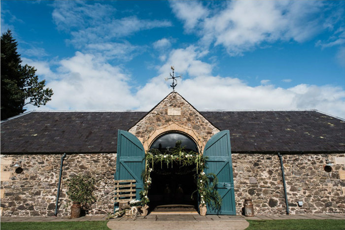 exterior photograph of the byre at inchyra with blue barn doors and floral arch