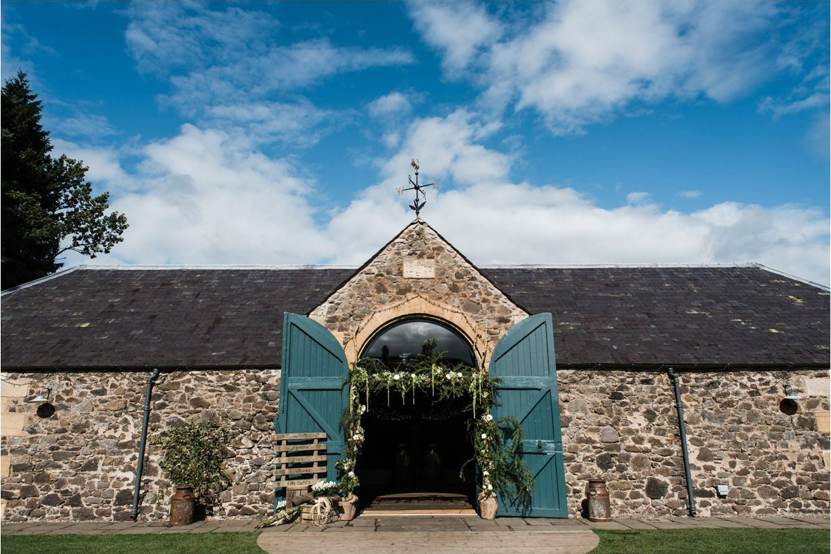 exterior photograph of the byre at inchyra with blue barn doors and floral arch