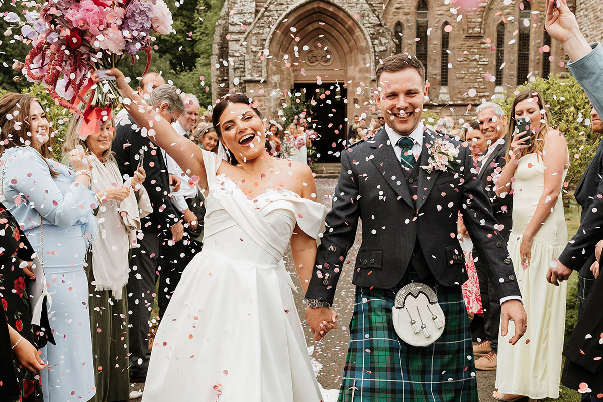 Bride and groom walking through confetti shower outside St Palladius Church at Drumtochty Castle Aberdeenshire