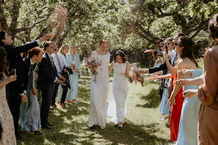 guests throw confetti at two brides during outdoor wedding at the Byre at Inchyra