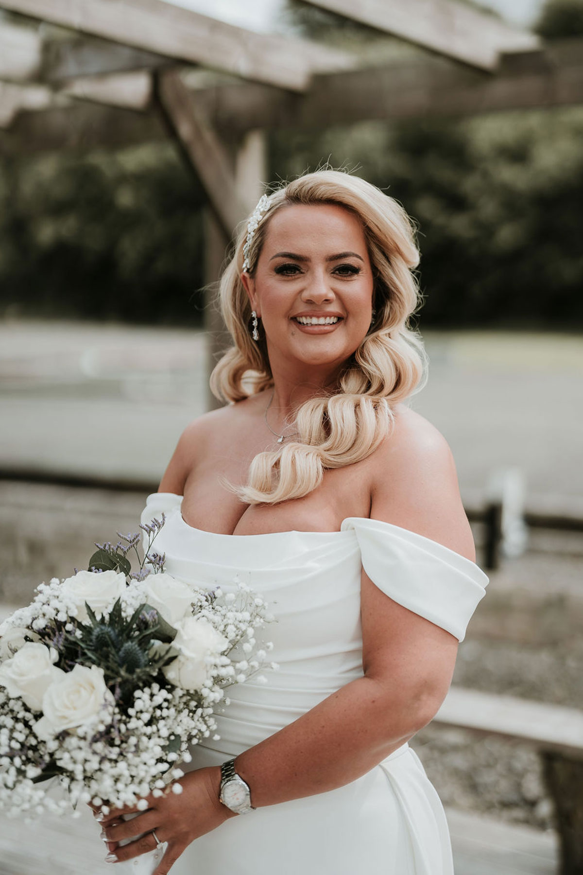 Bride smiling outdoors holding a white rose bouquet.