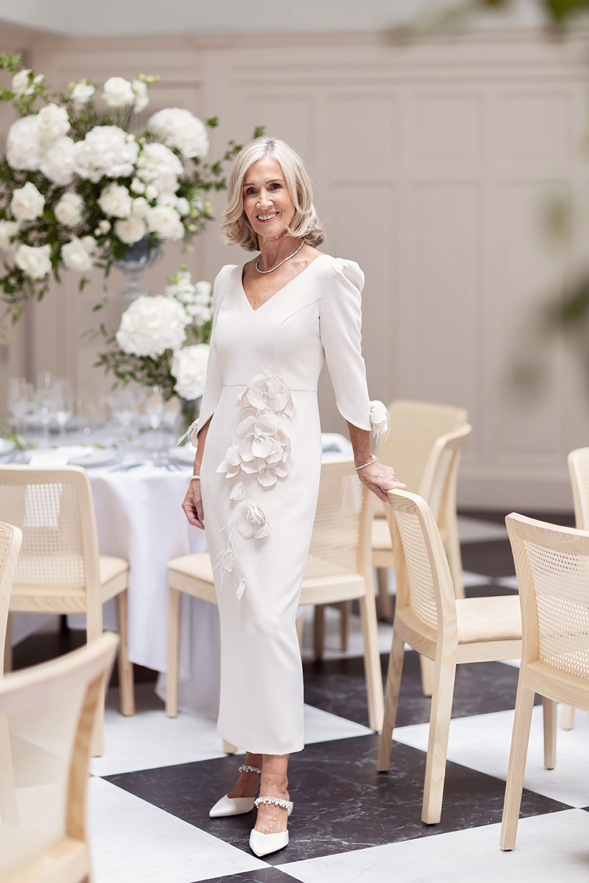 Mother of the bride in elegant ivory dress with floral appliqué, standing in decorated wedding venue