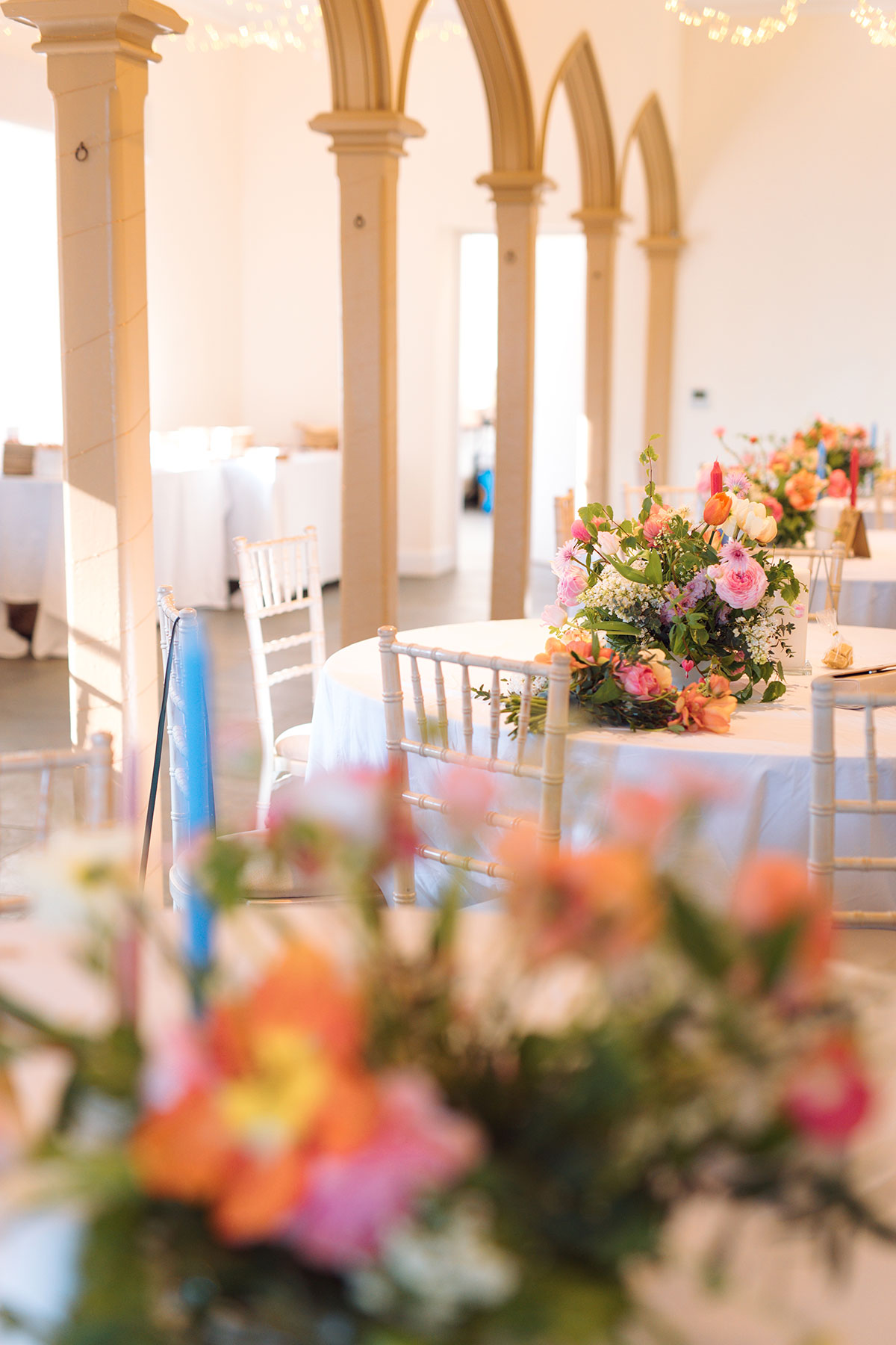 Wedding reception tables with floral centrepieces in light-filled room with arched columns