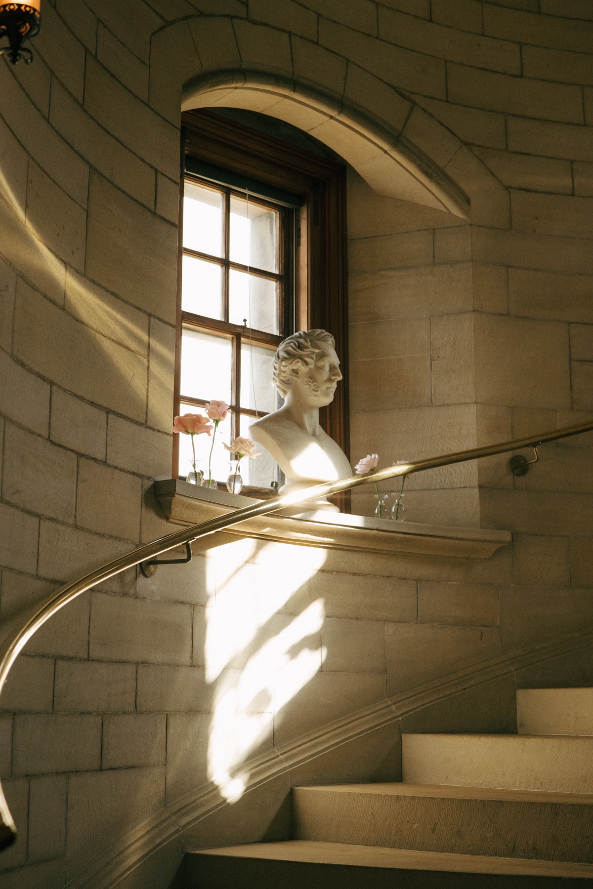 Sunlight illuminates a classical marble bust and delicate pink flowers on a stone staircase inside Barnbougle Castle in South Queensferry.