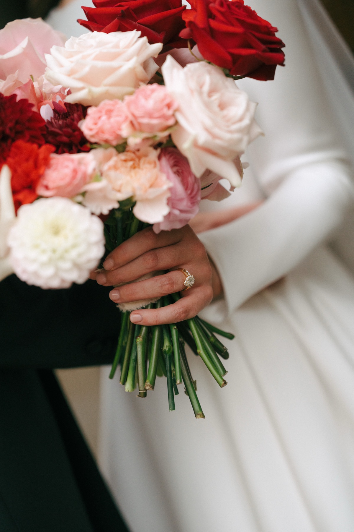 Close-up of Nicole's bridal bouquet featuring red, blush pink and ivory roses, with her engagement ring visible at Barnbougle Castle.