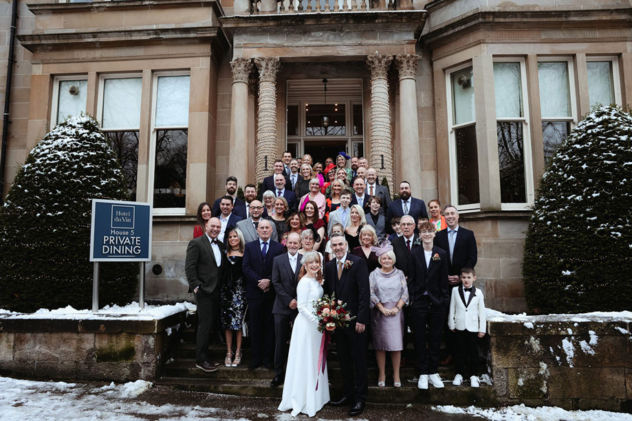 a group of wedding guests standing in front of a grand building on the front stairs 