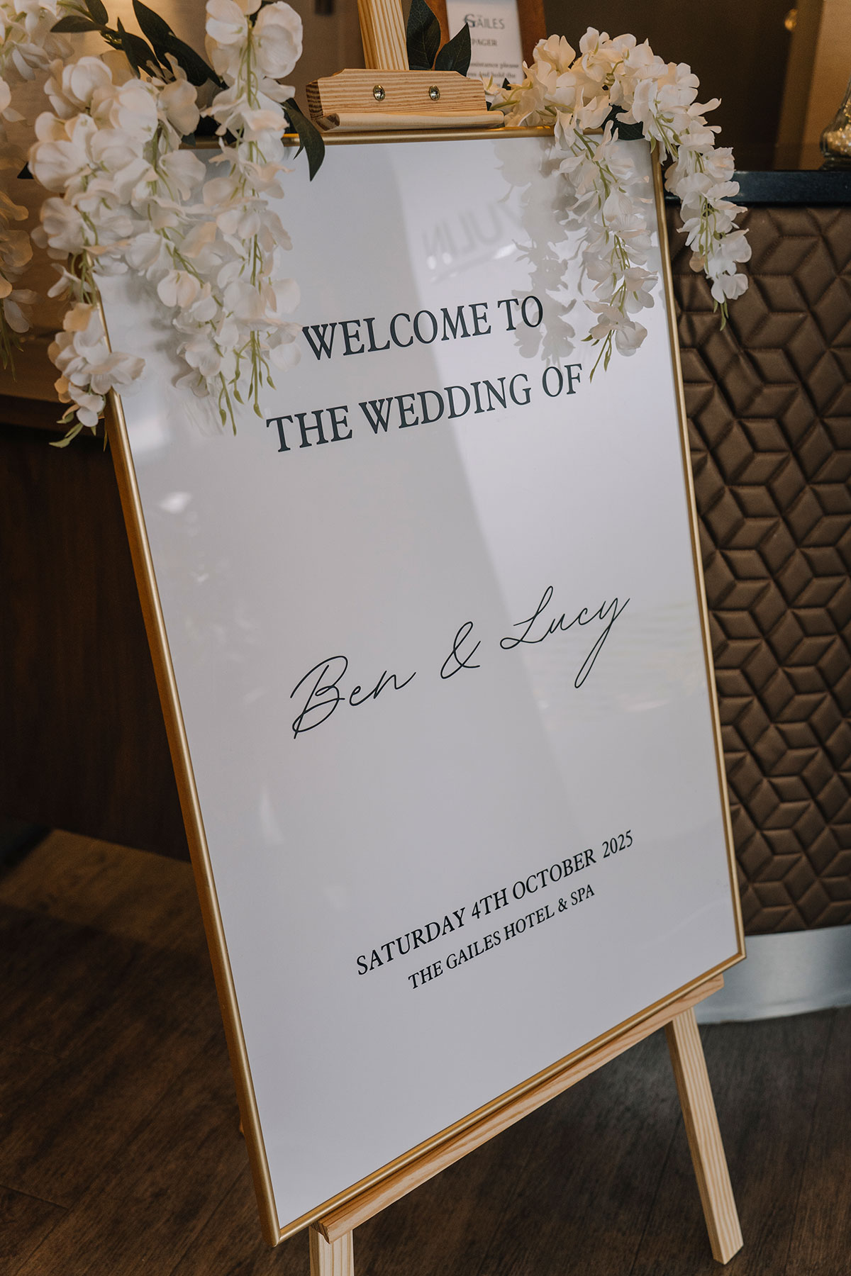 Gold-framed wedding welcome sign for Ben and Lucy displayed on an easel with white floral garlands at Gailes Hotel & Spa