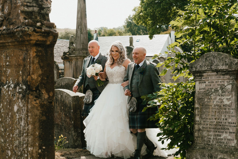 A Bride On The Arm Of Her Dad And Stepdad