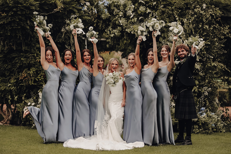 A Bride Poses In A Garden With A Man In A Kilt And 7 Bridesmaids Wearing Pale Blue Satin Dresses