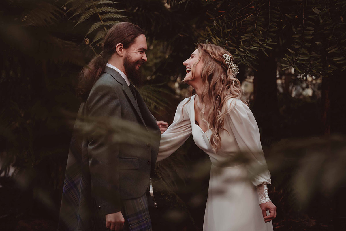 Bride and groom laughing together in woodland setting during relaxed outdoor wedding photoshoot in Scotland