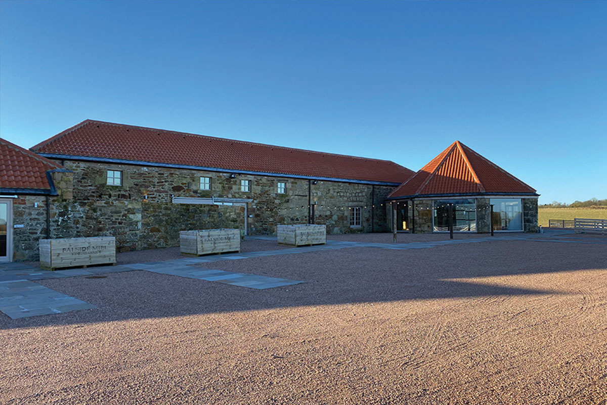 The exterior of a one storey stone building with a red roof