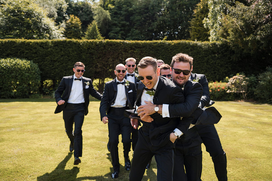Excited groomsmen laugh and play around on grass before ceremony