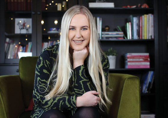 blonde smiling woman rests her fist under her chin while sat on green chair