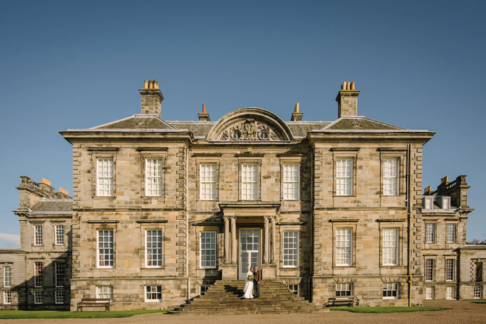 a stately home with a couple standing on the stairs in front of the house