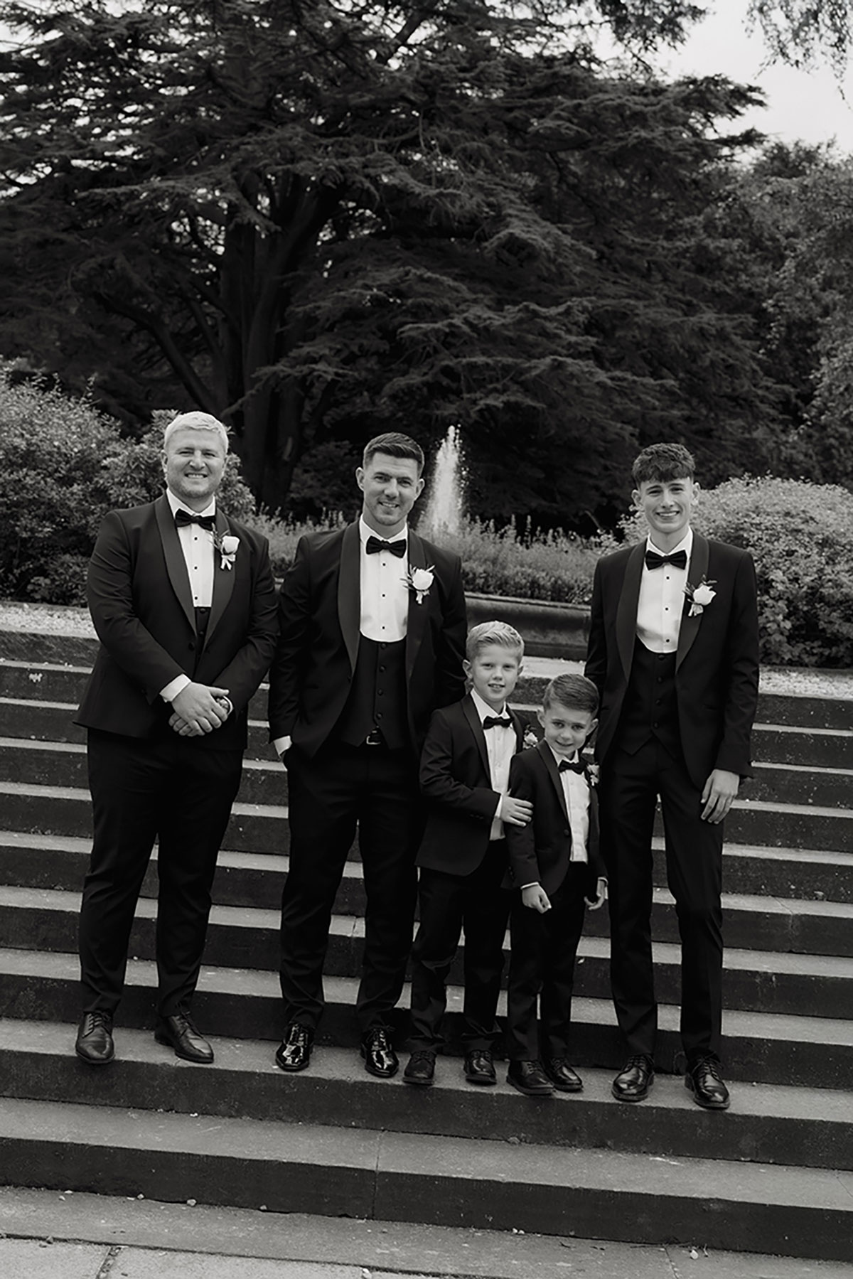 Groom and groomsmen, including two young pageboys, standing together on the steps at Mar Hall.