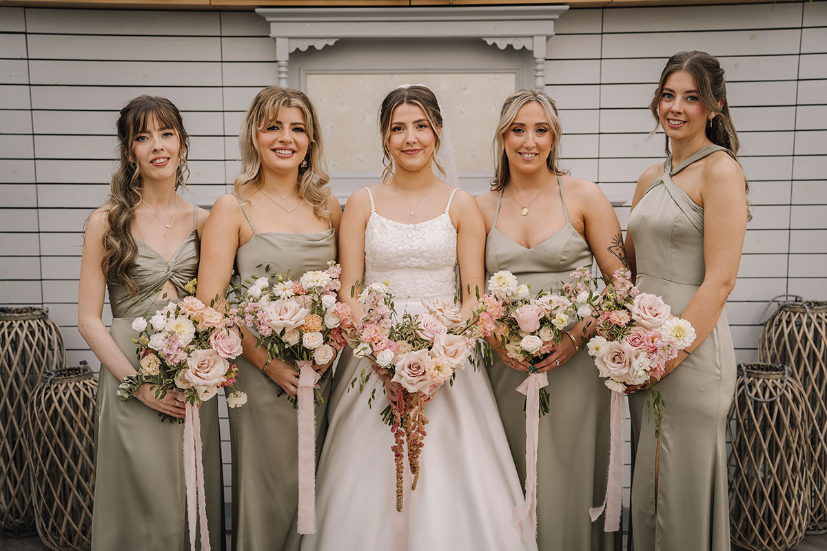 Bride standing with her bridesmaids in sage green dresses holding pastel floral bouquets during wedding portraits