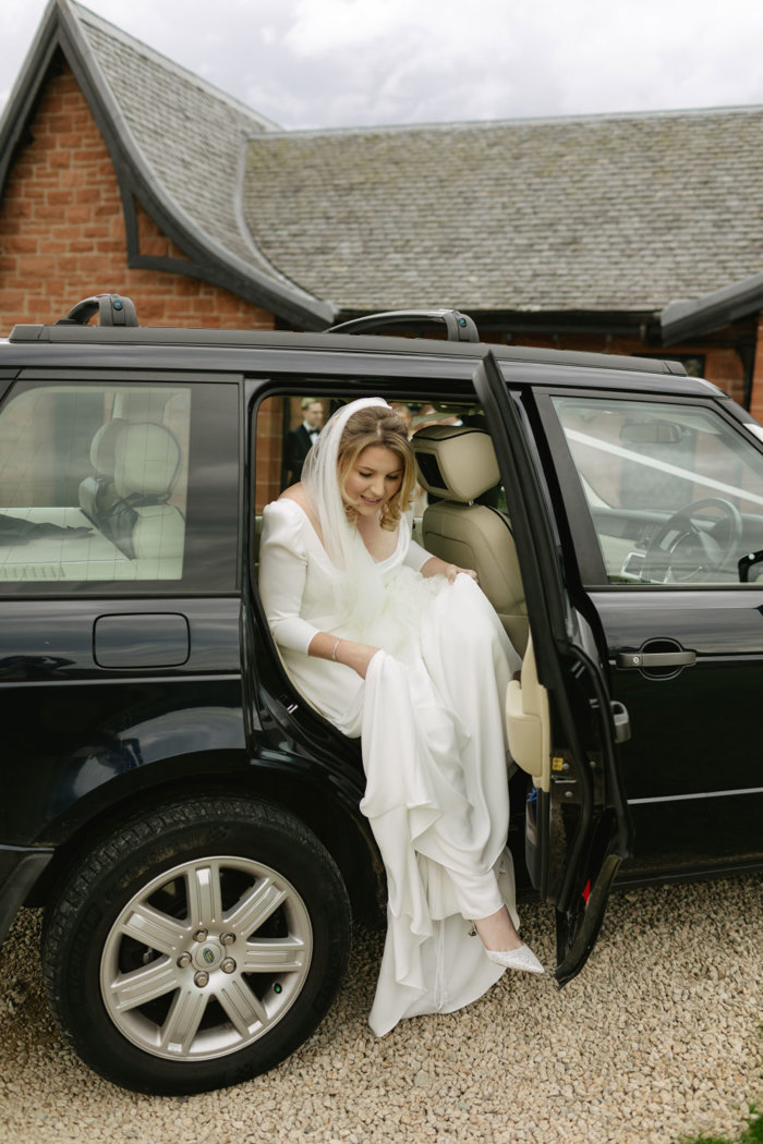 a bride stepping out of a black range rover vehicle in front of a red brick building with black pitched roof