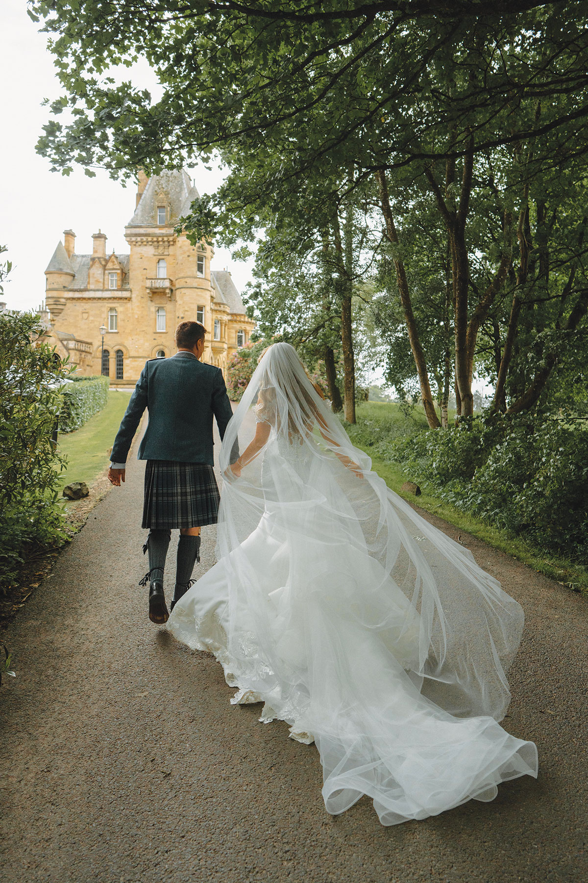 image of bride and groom walking towards cornhill castle as bride's veil blows in the wind
