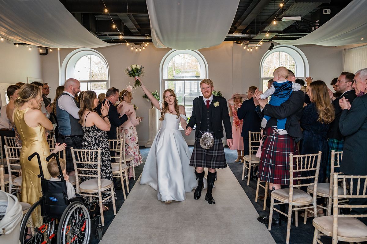 Newlyweds walking down aisle after ceremony at The Venue Eskmills with guests applauding