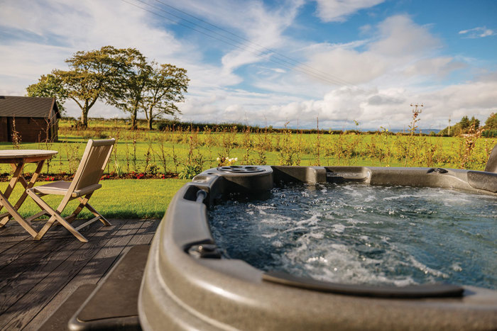 Outdoor hot tub on decking overlooking green fields and blue skies