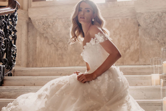 blonde woman in big off the shoulder wedding dress sitting on stair steps