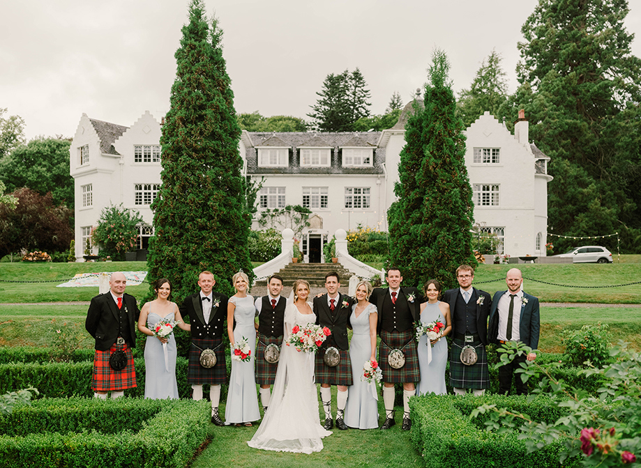 A bride and groom joined by their wedding guests in a garden in front of their venue