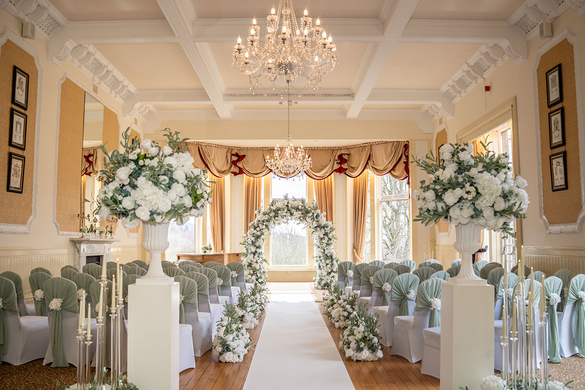 Wedding ceremony setup inside Atholl Palace Hotel featuring a white floral arch, elegant aisle décor, chandeliers and rows of guest seating