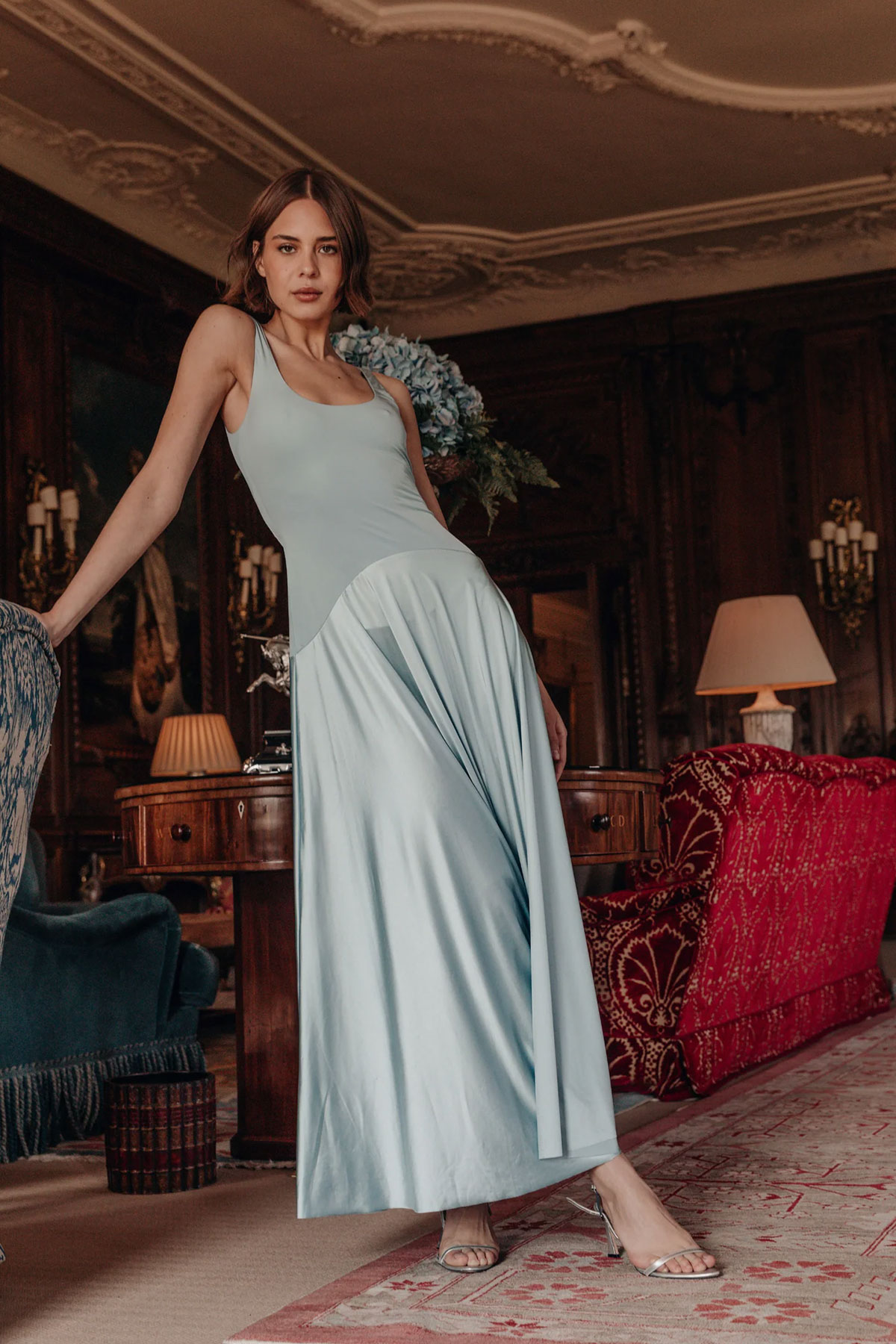 Pale blue satin maxi dress with fitted bodice and soft drape styled in a classic heritage interior
