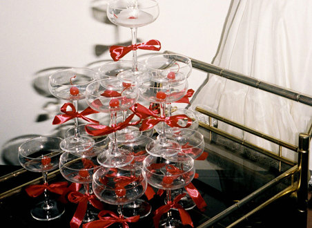 champagne tower of coupe glasses with red bows around the stems, all placed on a cocktail trolley
