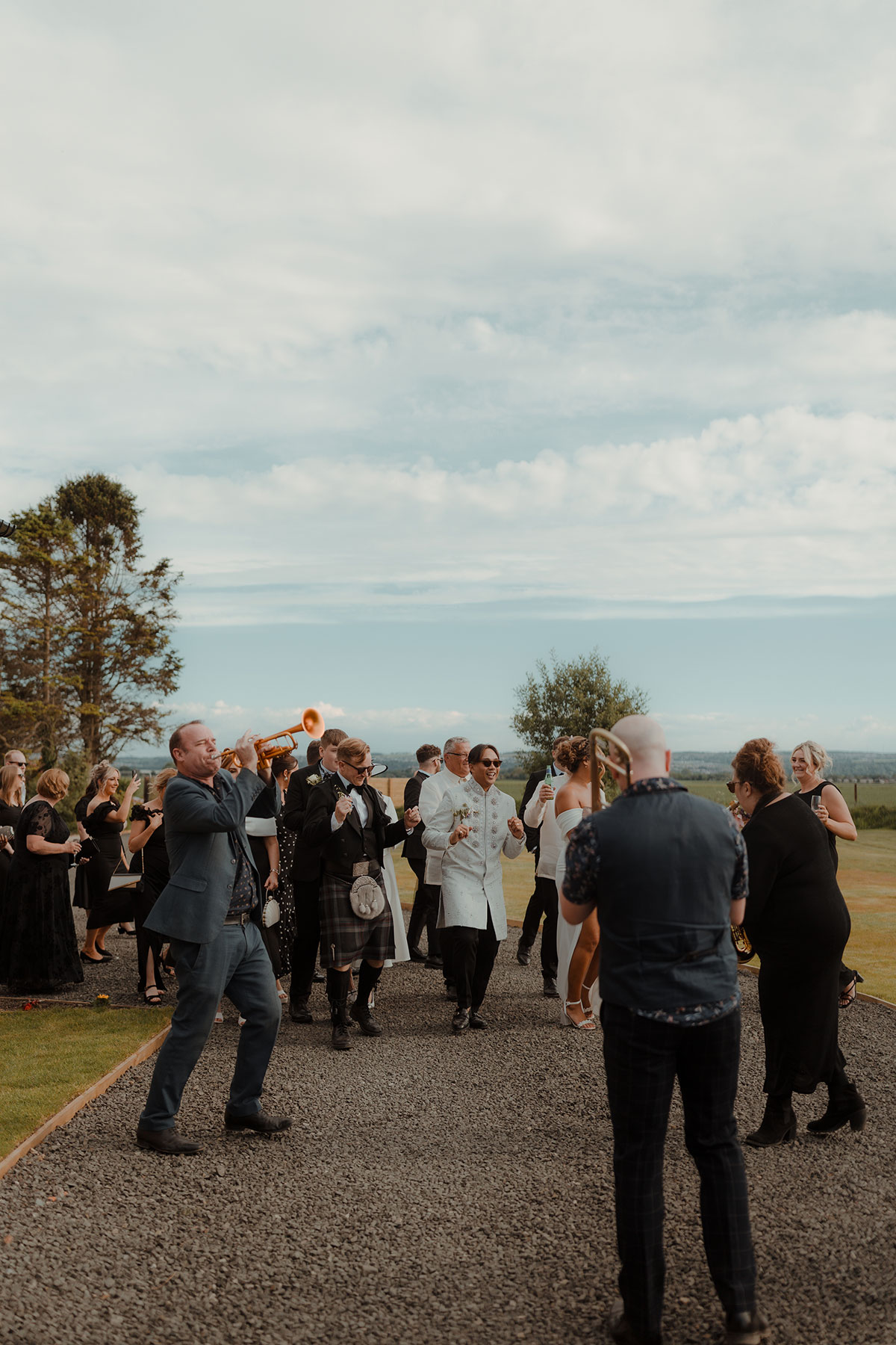 Wedding guests dancing behind a brass band during drinks reception at a farm wedding venue near Falkirk, Scotland