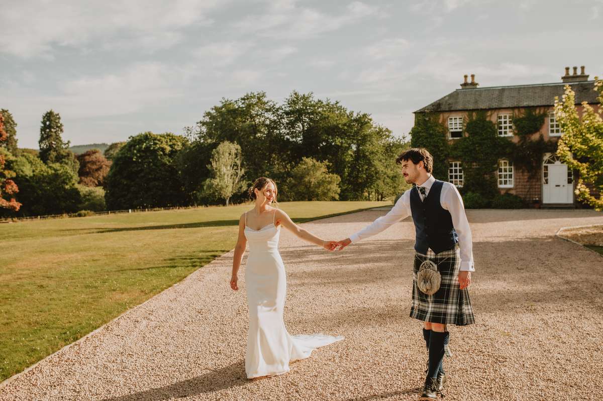 Bride and groom walk together along the gravel driveway outside Ballogie House